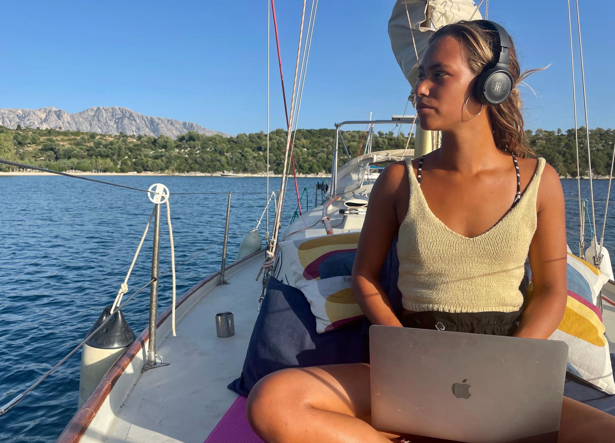 Virtual Assistant on a small sailboat in Greece, Apple MacBook Pro, Lau wearing headphones, on the ocean.