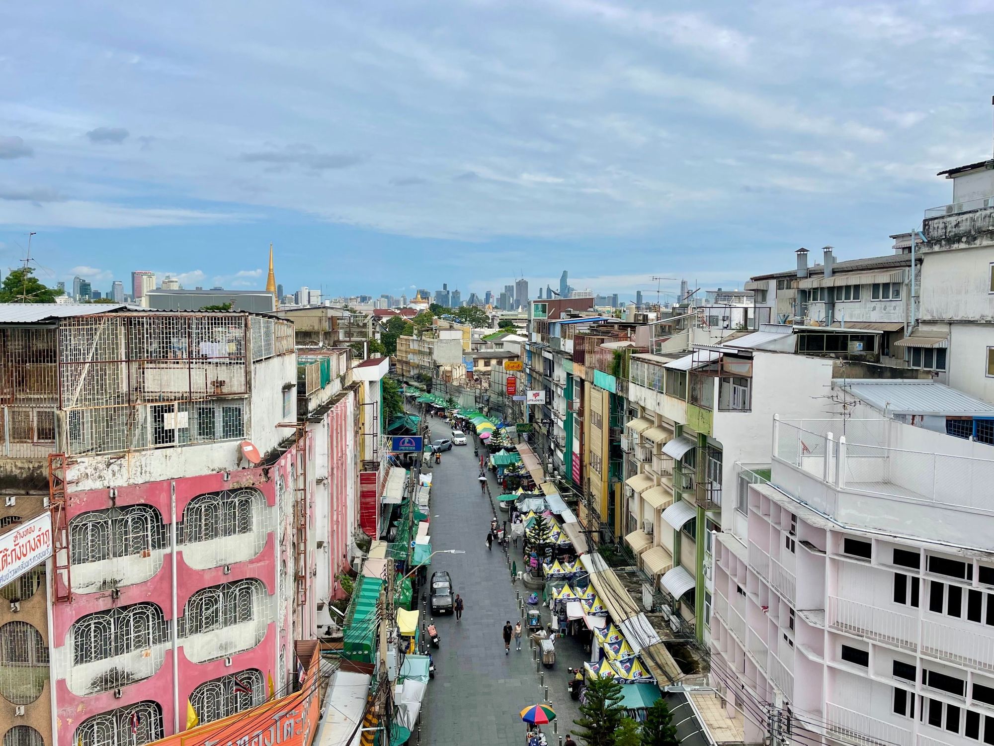 View of Bangkok city, Thailand of sunset Rooftop Bar at Liberta Hostel. Old thai buildings with skyscrapers in the background. Lots of stalls and tuktuks on the road.