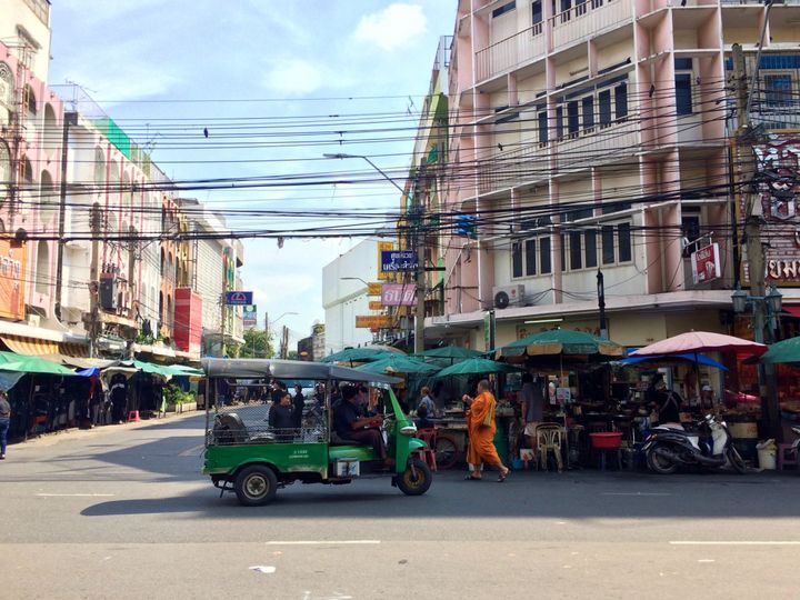 Streets of Bangkok, Thailand. A green tuktuk and a monk wearing orange walking past. 