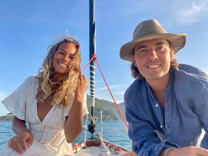 Iz and Lau sitting at the. bow of their sailboat Bellatrix, in Greece, blue sky, blue ocean